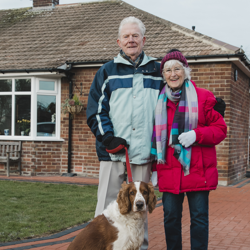 Photo of an older couple standing in front of their family home